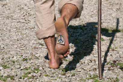 Mann barfuß unterwegs auf Steinweg mit Pilgerstock und Friedenszeichen auf der Fußsohle